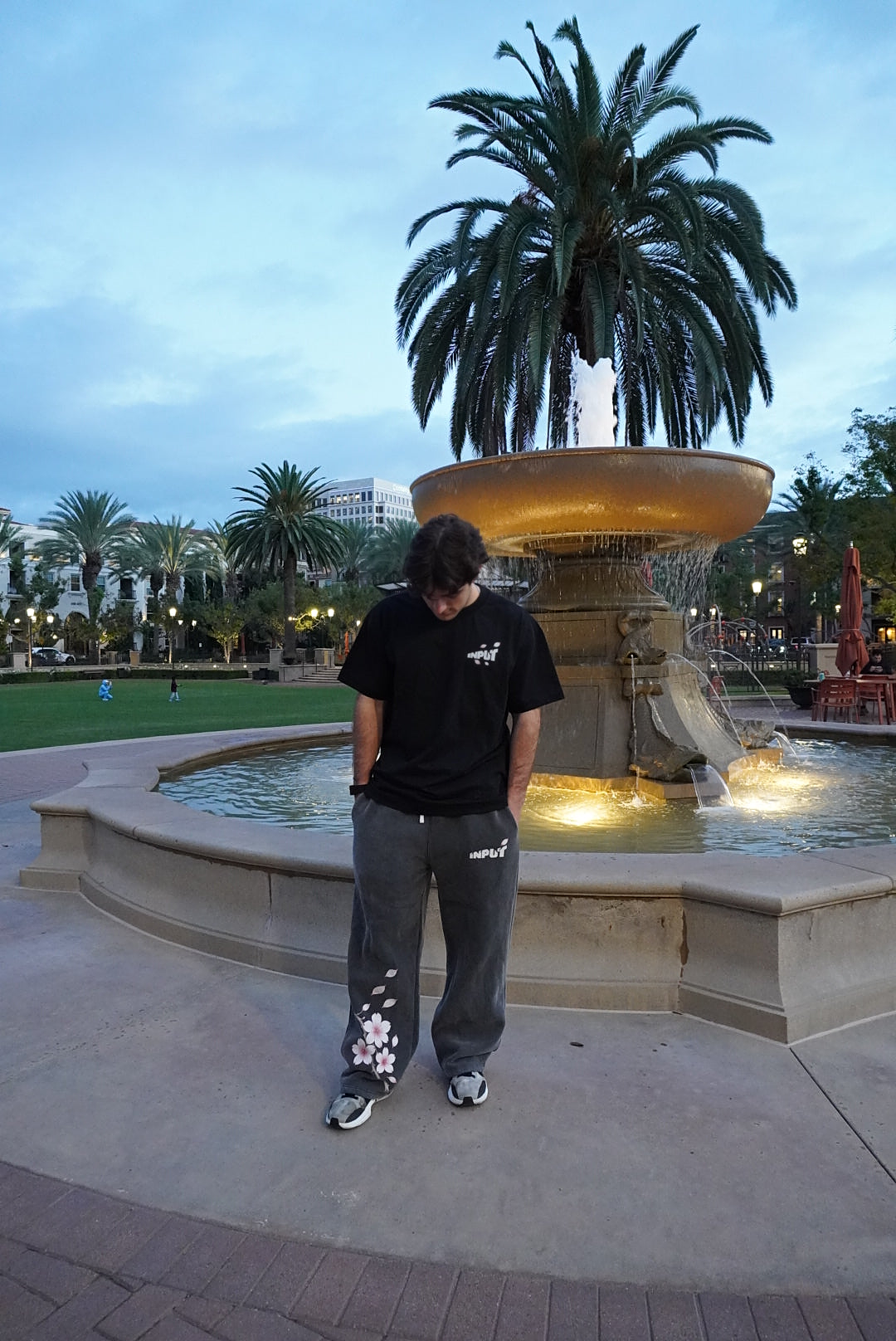INPUT wearer looking down beside the fountain, shown from head to shoes